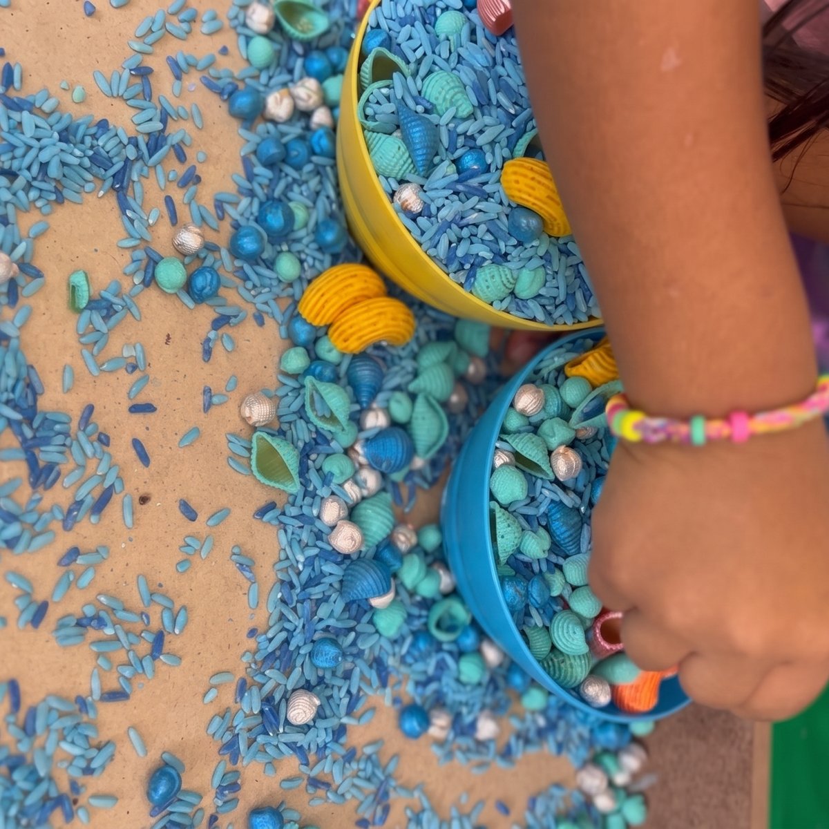 Mano de niña jugando con arroz y pasta de colores