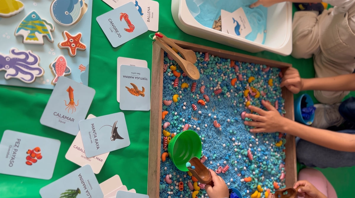 Niños explorando una bandeja sensorial con arroz de colores y tarjetas del océano