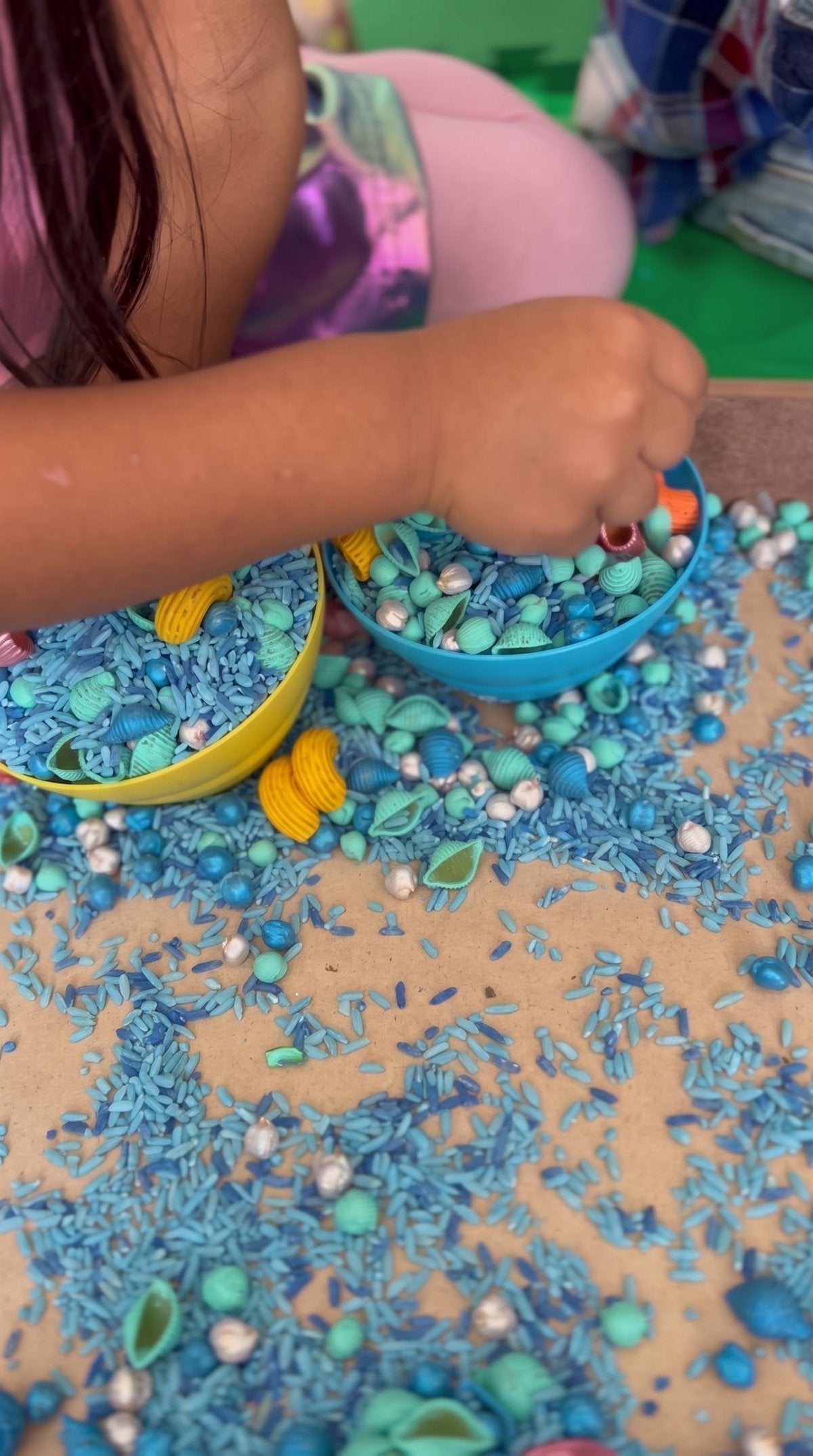 Niña llenando un recipiente con arroz y pasta de colores
